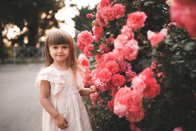 Jolie petite fille avec des fleurs roses en fleurs dans un parc à l'extérieur