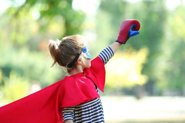 Photo jolie petite fille habillée en super-héros dans des gants de boxe au parc