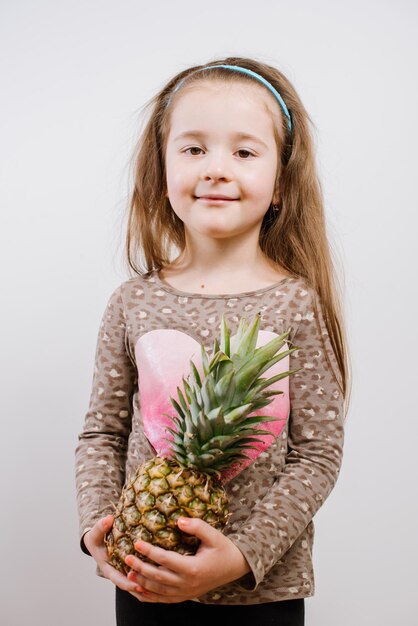 Jolie petite fille heureuse tenant un ananas sur fond gris