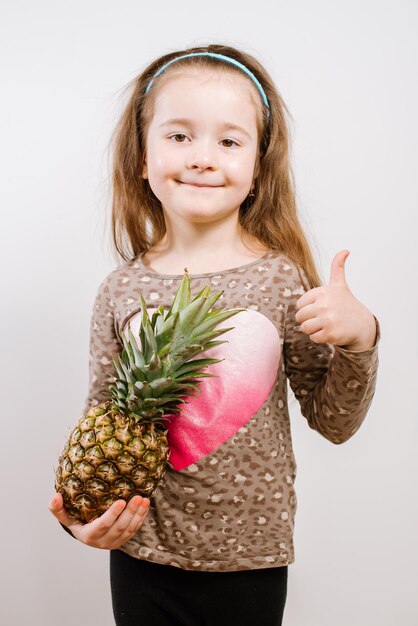 Jolie petite fille heureuse tenant un ananas sur fond gris