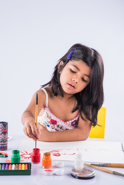 Jolie petite fille indienne ou asiatique appréciant la peinture à la maison avec du papier, de l'aquarelle et un pinceau d'art. Mise au point sélective