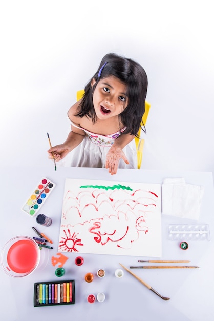 Jolie petite fille indienne ou asiatique appréciant la peinture à la maison avec du papier, de l'aquarelle et un pinceau d'art. Mise au point sélective