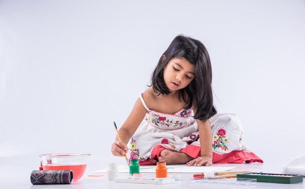 Jolie petite fille indienne ou asiatique appréciant la peinture à la maison avec du papier, de l'aquarelle et un pinceau d'art. Mise au point sélective