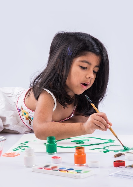 Jolie petite fille indienne ou asiatique appréciant la peinture à la maison avec du papier, de l'aquarelle et un pinceau d'art. Mise au point sélective