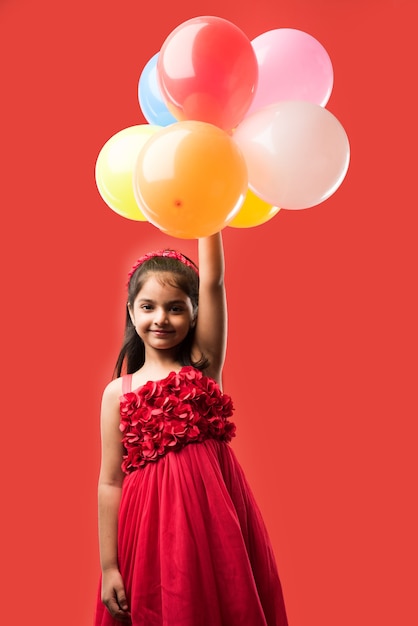 Jolie petite fille indienne ou asiatique avec des ballons colorés ou du gubbare en hindi, sur fond blanc ou rouge
