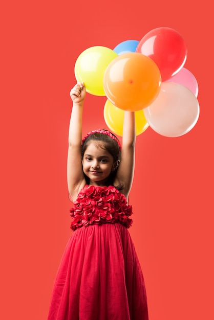 Jolie petite fille indienne ou asiatique avec des ballons colorés ou du gubbare en hindi, sur fond blanc ou rouge