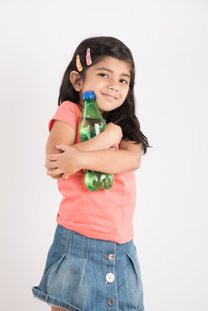 Jolie petite fille indienne ou asiatique avec une bouteille pour animaux de compagnie de boisson froide à l'orange ou à la mangue ou de jus de fruits, buvant ou tenant debout isolé sur fond bleu ou blanc.