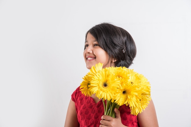 Jolie petite fille indienne tenant un bouquet ou un bouquet de fleurs de gerbera jaunes fraîches. Isolé sur fond blanc