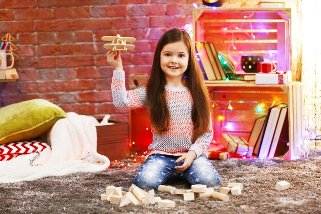 Jolie petite fille jouant avec un avion en bois dans une chambre décorée de Noël