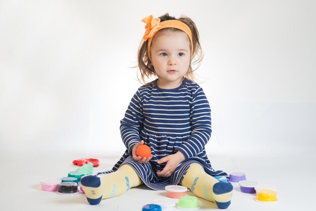 Jolie petite fille jouant avec de la pâte à modeler colorée sur fond blanc