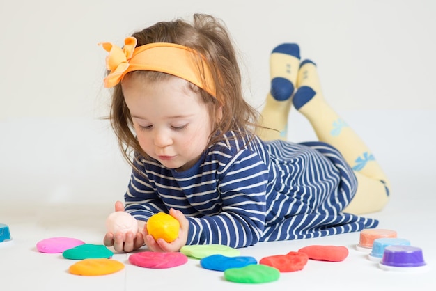 Jolie petite fille jouant avec de la pâte à modeler colorée sur fond blanc