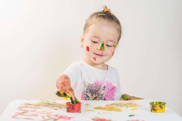 Jolie petite fille jouant avec des peintures colorées sur fond blanc