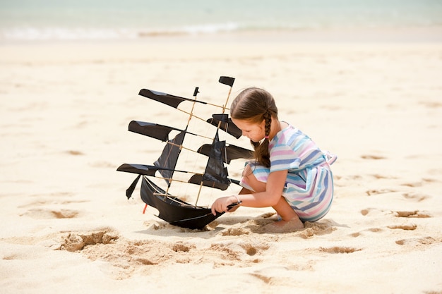Jolie petite fille jouant sur la plage cerf-volant de bateau volant