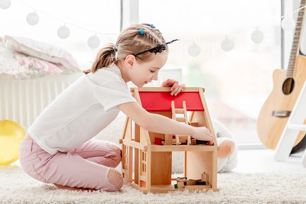 Jolie petite fille joue avec une maison de poupée en bois dans la chambre des enfants