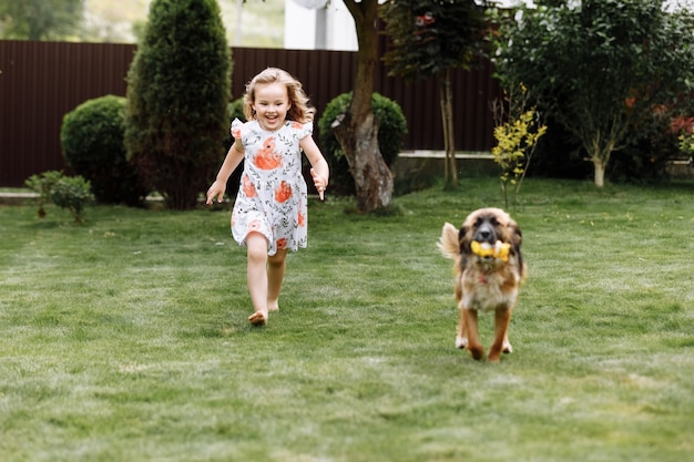 Une jolie petite fille joue avec son chien à l'extérieur sur l'herbe à la maison