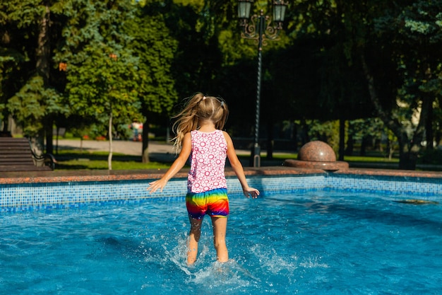 Jolie petite fille joyeuse joue dans la fontaine. L'enfant s'amuse dans un parc d'été dans la fontaine de la ville.