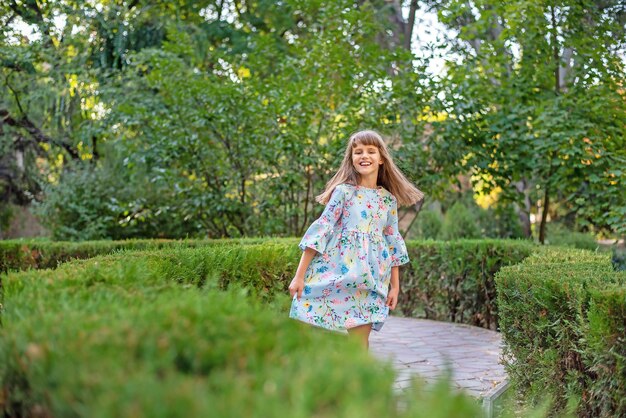 Une jolie petite fille joyeuse joue dans un labyrinthe vert de buissons.