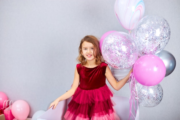 Jolie petite fille joyeuse en robe rose et chapeau jouant avec des ballons à la fête d'anniversaire à la maison