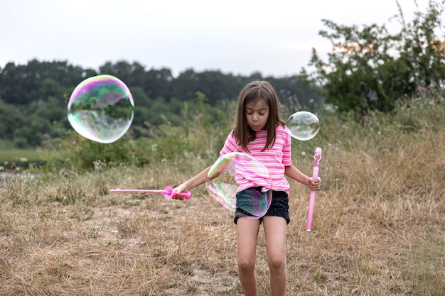 Une jolie petite fille lance d'énormes bulles de savon en arrière-plan une belle nature.