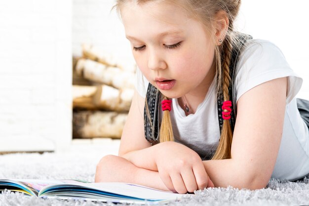 Jolie petite fille lit un livre sur un tapis dans un appartement