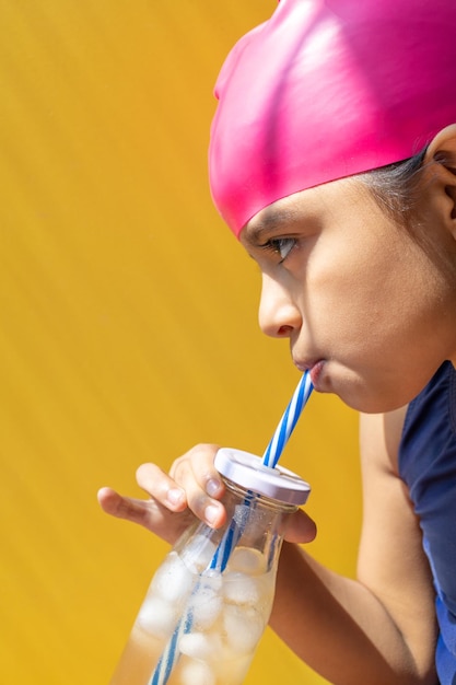 Jolie petite fille en maillot de bain prenant un bain de soleil tout en buvant une limonade