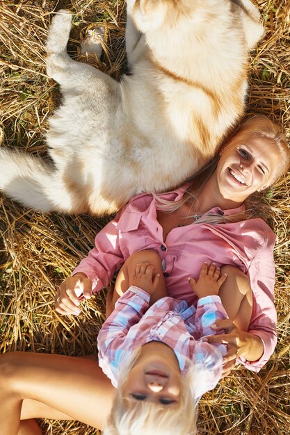 Jolie petite fille avec maman et chien sur le champ de blé. Une jeune famille heureuse passe du temps ensemble dans la nature. Maman, petite fille et chien husky se reposant à l'extérieur. unité, amour, concept de bonheur.