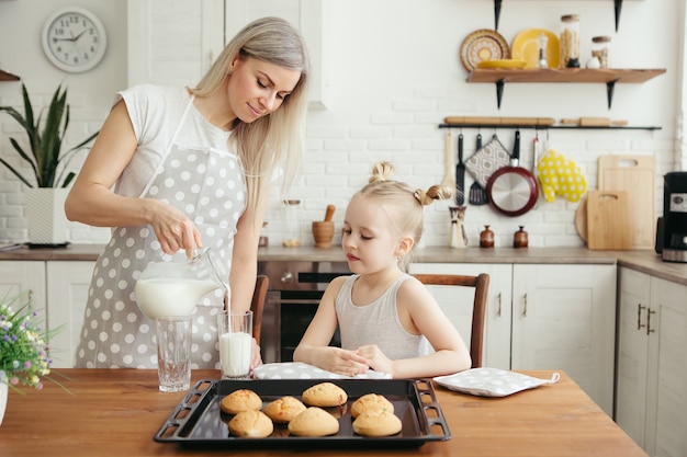 Jolie petite fille et maman mangeant des biscuits fraîchement préparés avec du lait dans la cuisine. Famille heureuse. Tonifiant.