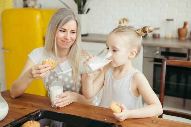 Jolie petite fille et maman mangeant des biscuits fraîchement préparés avec du lait dans la cuisine. Famille heureuse. Tonifiant.