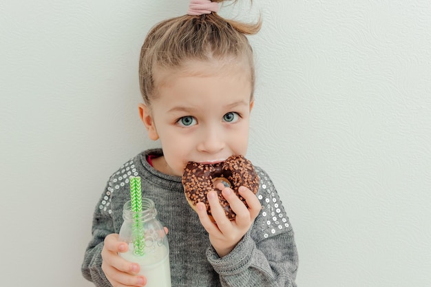 Jolie petite fille mange un beignet au chocolat avec une bouteille de lait