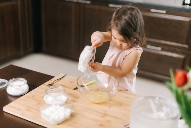 Jolie petite fille met le fromage cottage dans un bol pour faire des gâteaux au fromage