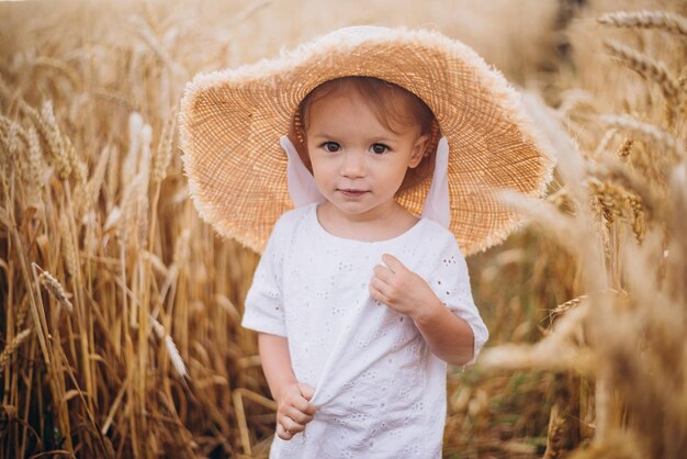 Photo jolie petite fille mignonne avec un beau sourire portant un chapeau de paille d'été lors d'une promenade dans les champs de blé mise au point sélective concept de famille