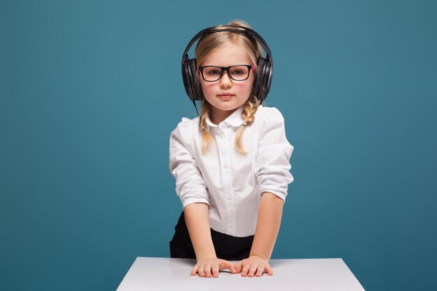 Jolie petite fille mignonne en chemise blanche, lunettes, pantalon noir et casque