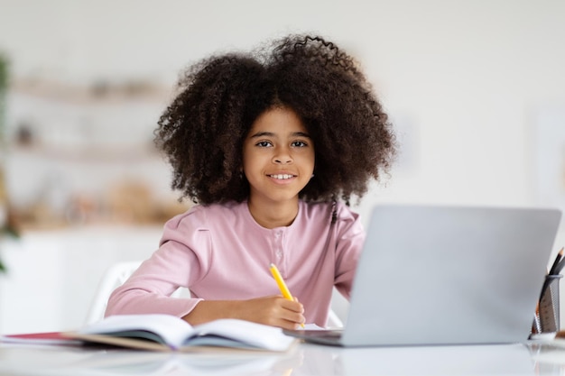 Jolie petite fille noire faisant ses devoirs à l'aide d'un ordinateur