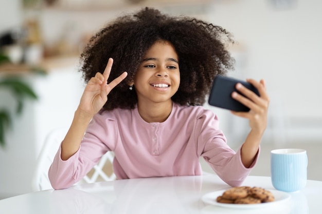 Jolie petite fille noire prenant un selfie à l'aide d'un smartphone