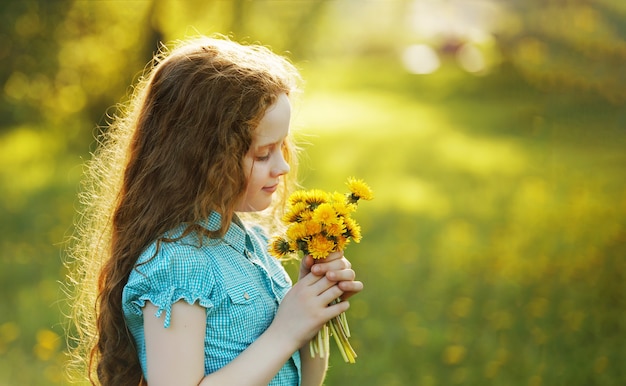 Jolie petite fille avec des pissenlits jaunes sur le terrain.