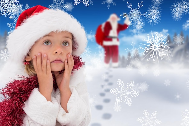 Jolie petite fille portant un bonnet de noel et des guirlandes contre un ciel bleu vif au-dessus des nuages