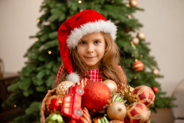 Jolie petite fille portant un bonnet de Noel tout en tenant un panier avec des décorations de Noël