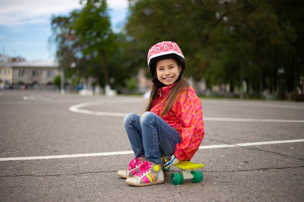 Jolie petite fille portant un casque à cheval sur une planche à roulettes dans un magnifique parc d'été