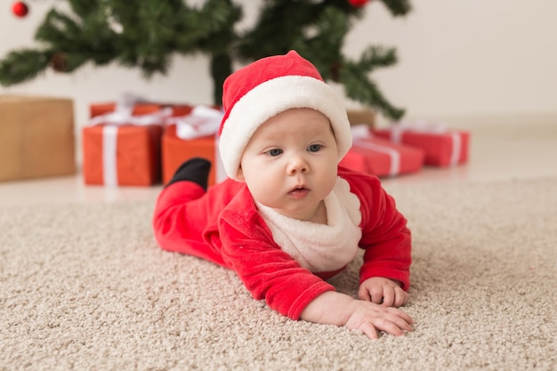 Jolie petite fille portant un costume de père Noël rampant sur le sol au-dessus de l'arbre de Noël. Saison des fêtes.