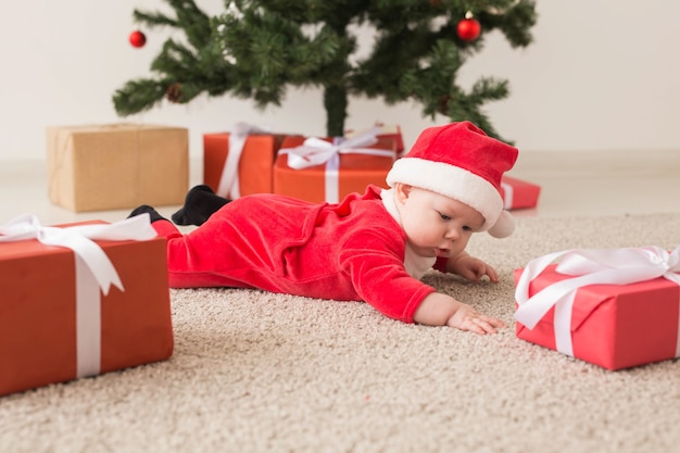 Jolie petite fille portant un costume de père Noël rampant sur le sol au-dessus de l'arbre de Noël. Saison des fêtes.