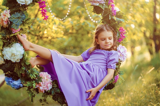 Jolie petite fille portant une robe lilas posant assis dans un anneau décoré de fleurs au parc l'été