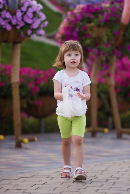 jolie petite fille avec une poupée dans les mains dans un beau jardin fleuri