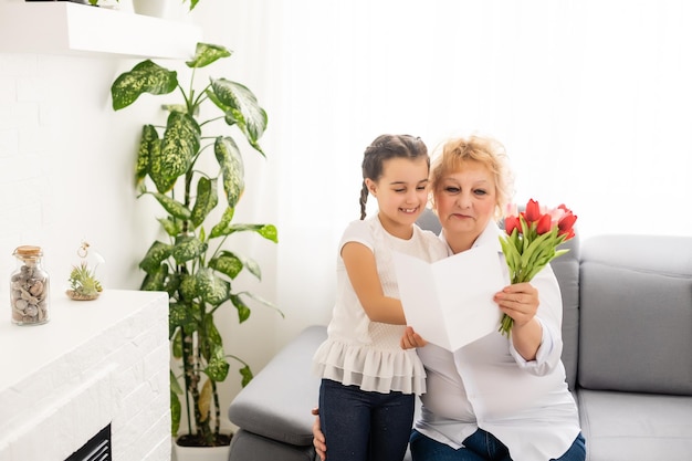 Jolie petite fille présentant un bouquet à sa grand-mère dans une salle lumineuse.