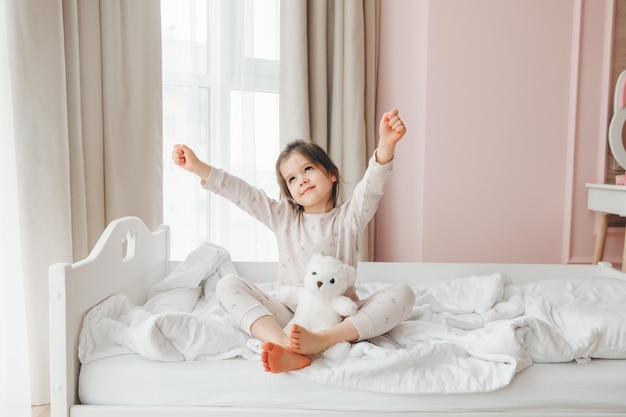 Une jolie petite fille profite d'une matinée ensoleillée Bonjour à la maison Une petite fille se réveille sur un lit avec un ours en peluche