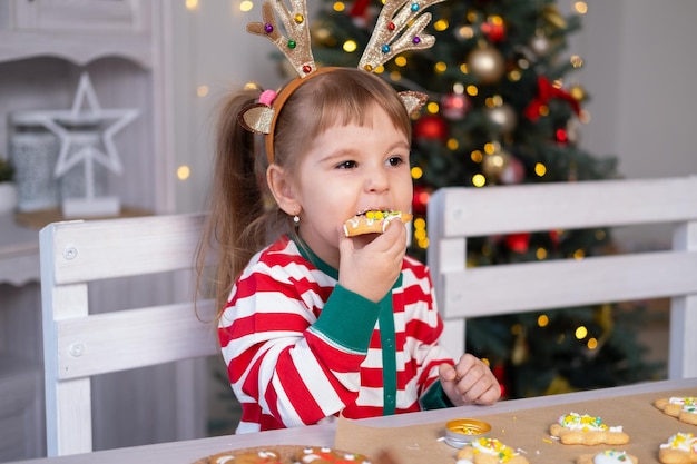 jolie petite fille en pyjama de Noël mangeant des biscuits assis dans la cuisine. période de Noël