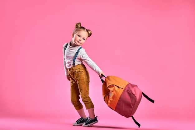 Photo jolie petite fille ramasse la sangle pour le sac à dos isolé sur fond rose espace de copie