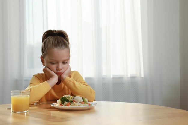 Jolie petite fille refusant de manger de la salade de légumes à la maison espace pour le texte