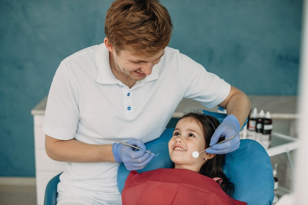 Jolie petite fille regardant son dentiste en souriant avant de faire un examen des dents.