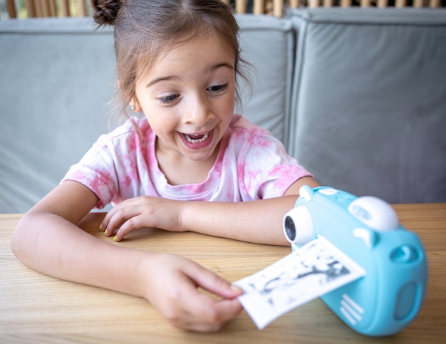 Une jolie petite fille regarde l'appareil photo bleu de ses enfants pour une impression photo instantanée.