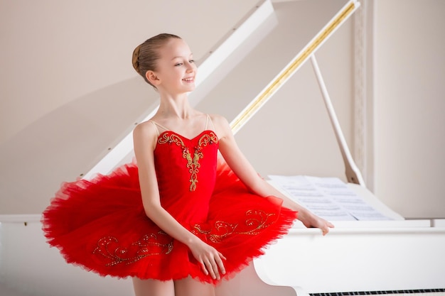 Une jolie petite fille rêve de devenir une ballerine professionnelle Dans une salle blanche, il se tient au piano dans un sac rouge vif Élève de l'école professionnelle